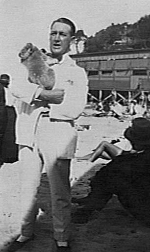 Man holding a koala on Manly Beach, surf pavilion in background
