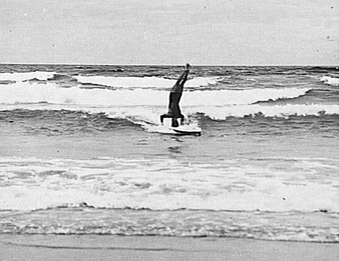 Man doing a head-stand on a surfboard, Freshwater Beach