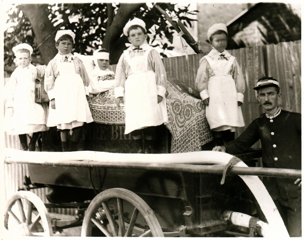 Fireman standing beside five children on fire brigade handcart