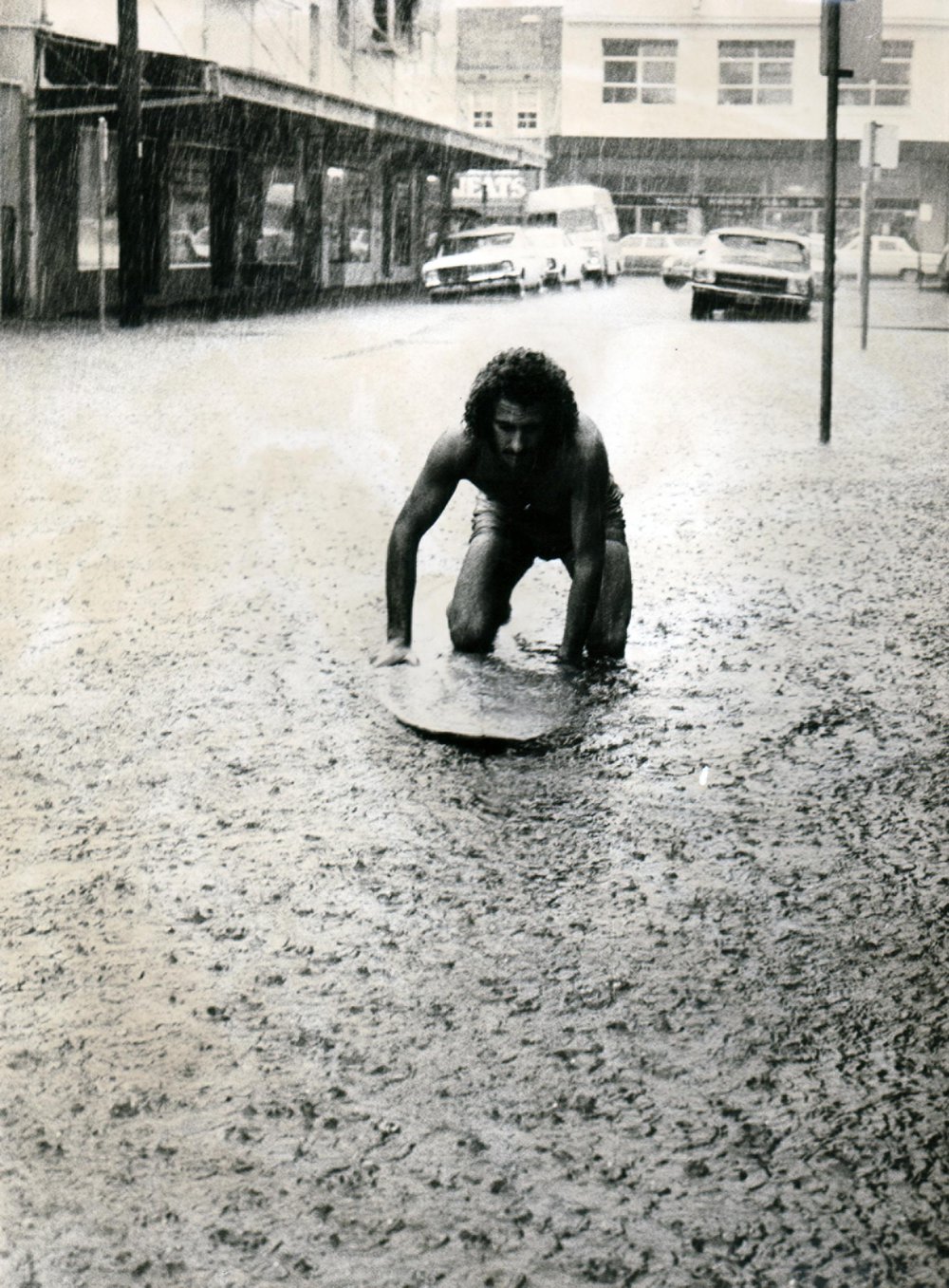 Surfboard rider in flooded Central Avenue, Manly 1970s