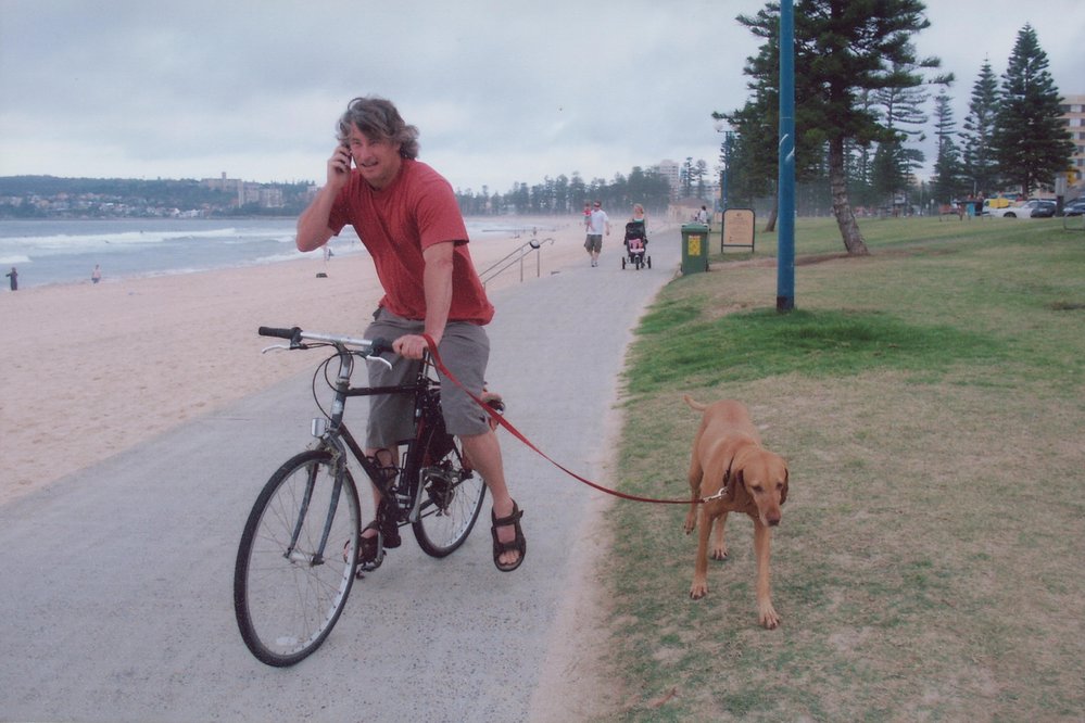 Man on bike talking on phone while leading dog, Queenscliff Beach, 2005