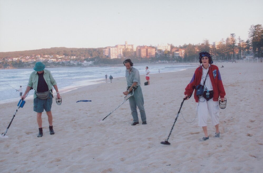 Three people sweeping the sand with metal detectors, with South Steyne Beach in background, Manly Beach, 2005