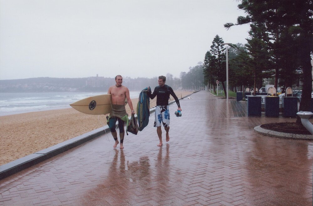 Two surfers walking home in the rain along the esplanade, Manly Beach, 2005