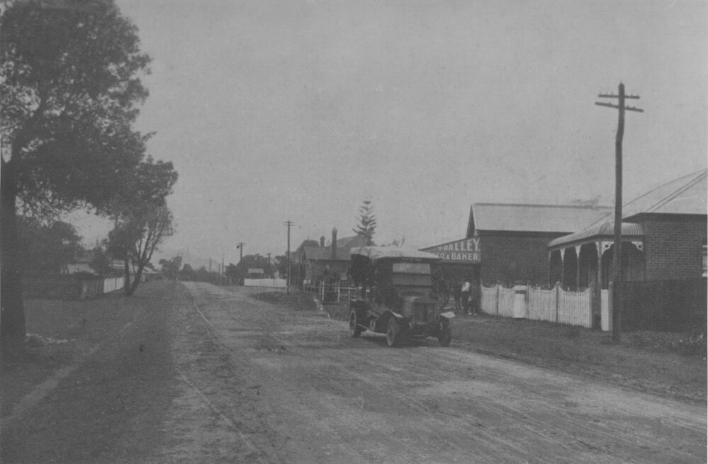 A street with vintage motor vehicle in front of H. Dalley Baker's Shop