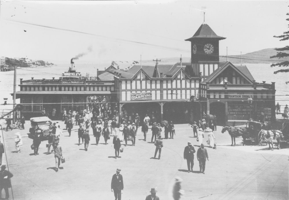 View across the Manly Wharf forecourt, showing crowds, the Edwardian facade and Clock Tower, Manly, c1922