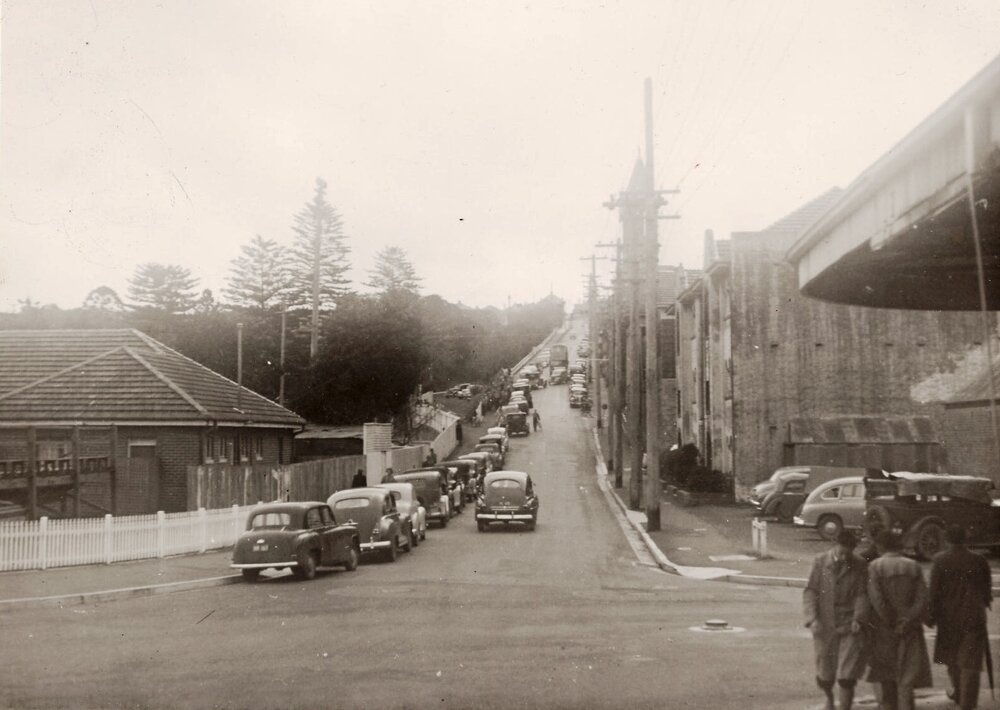 Cars parked up Raglan Street, a rugby match being played on Manly Oval, Manly, 29th June 1950