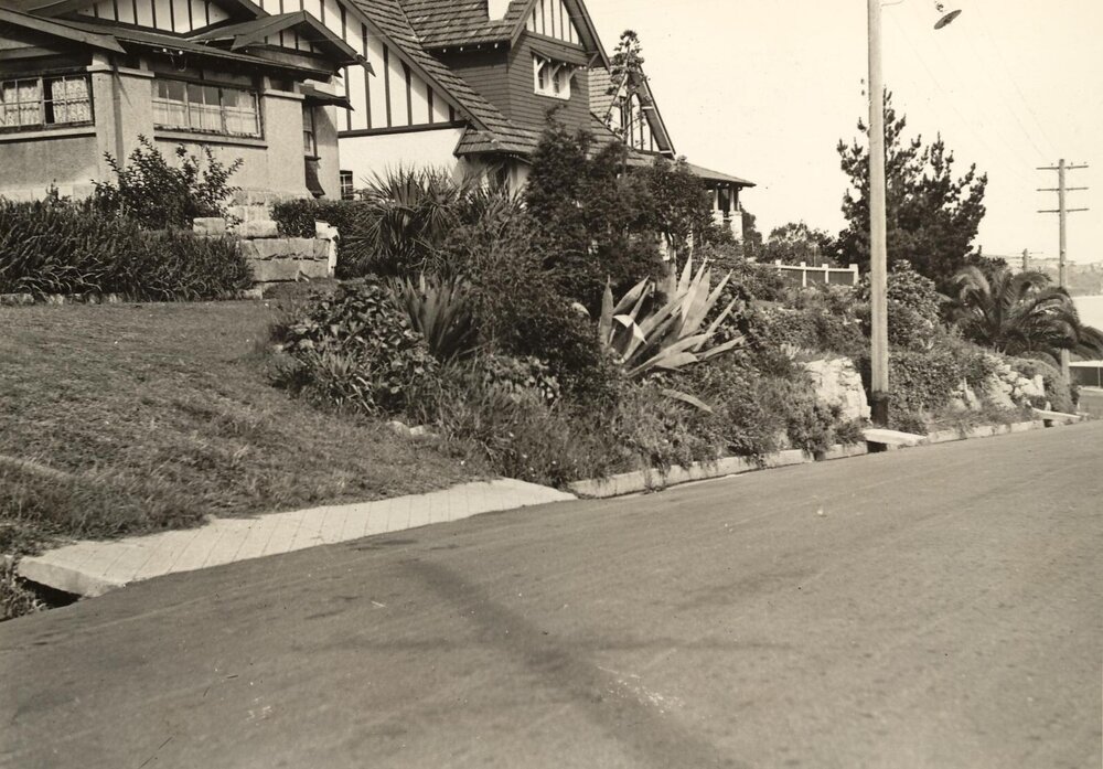 Front garden beds of two houses showing street drainage in foreground, c1940s