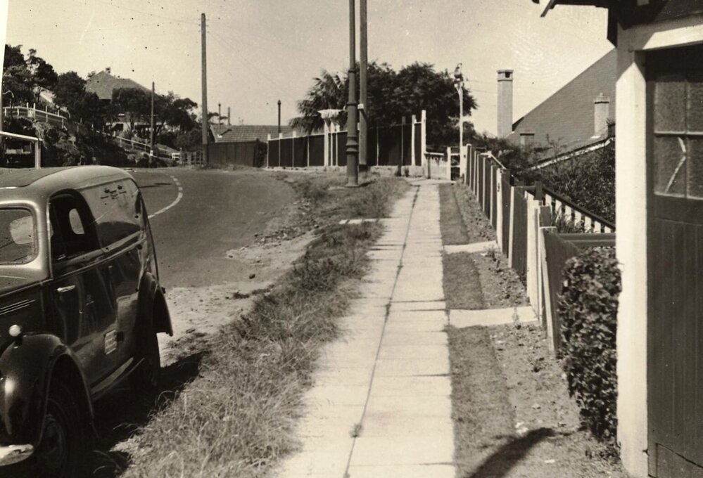 Unfinished footpath on unknown street, with parked car, c1940s