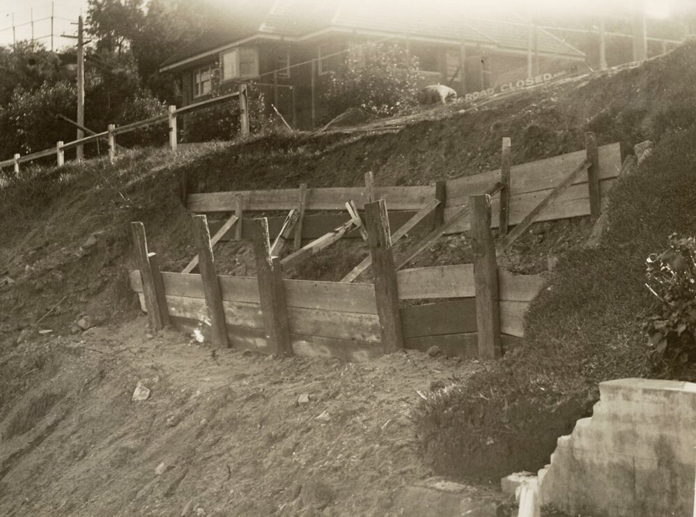 Construction works continue below road on steep slope with timber retaining wall, c1940s
