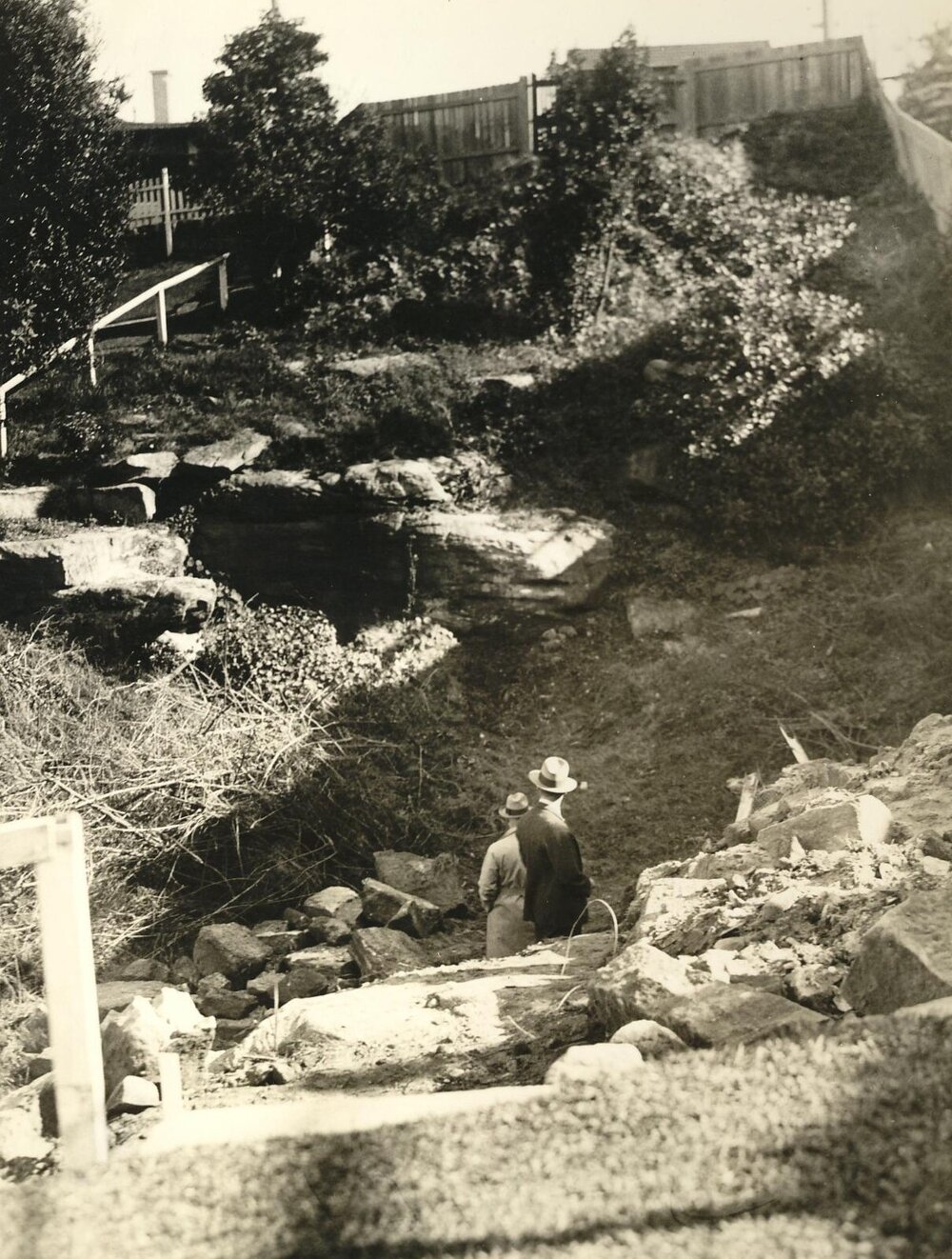 Two men surveying an unidentified worksite from bottom of a gully, c1940s