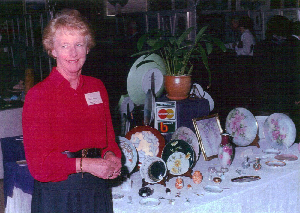 Diana Woolley, porcelain painter, standing in front of stall at Pittwater Arts &amp; Crafts Show, Mona Vale, 1972