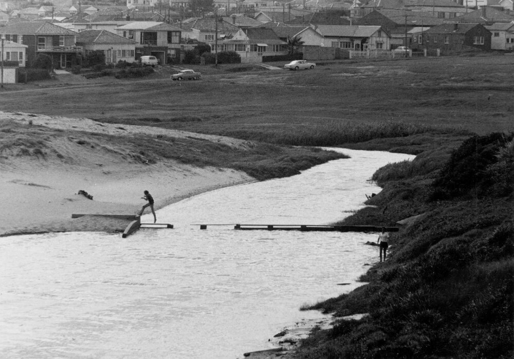 Person crossing narrow broken footbridge at Curl Curl Lagoon, Curl Curl, c1967-1973