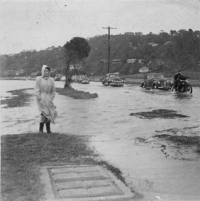 Coby Klerks standing on Pittwater Road showing the flooded streets at North Narrabeen, 1954 