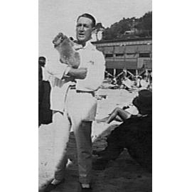 Man holding a koala on Manly Beach, surf pavilion in background