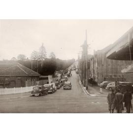 Cars parked up Raglan Street, a rugby match being played on Manly Oval, Manly, 29th June 1950