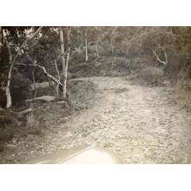Photograph of an unidentified unsealed road, showing sharp bend and slope c1940s