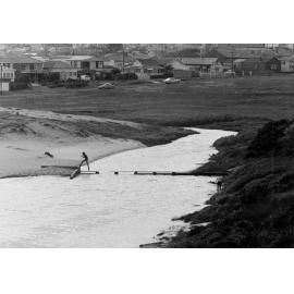 Person crossing narrow broken footbridge at Curl Curl Lagoon, Curl Curl, c1967-1973
