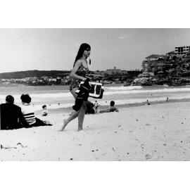 A woman walking across the Manly beach at South Steyne, Manly,  c1967–1973