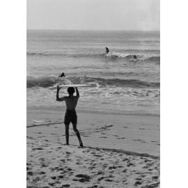 Surfer heading into the water at Manly Beach, Manly, 1972